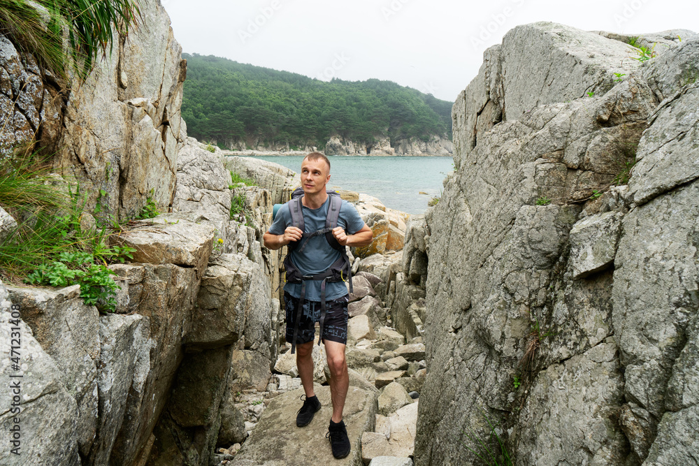 Active male backpacker hiking on cliff mountain enjoying trekking having summer leisure activity