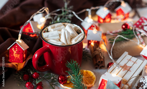 Winter hot drink, cacao with marshmallows and cinnamon or spicy hot chocolate in red cup and Christmas garland. Festive vintage background.