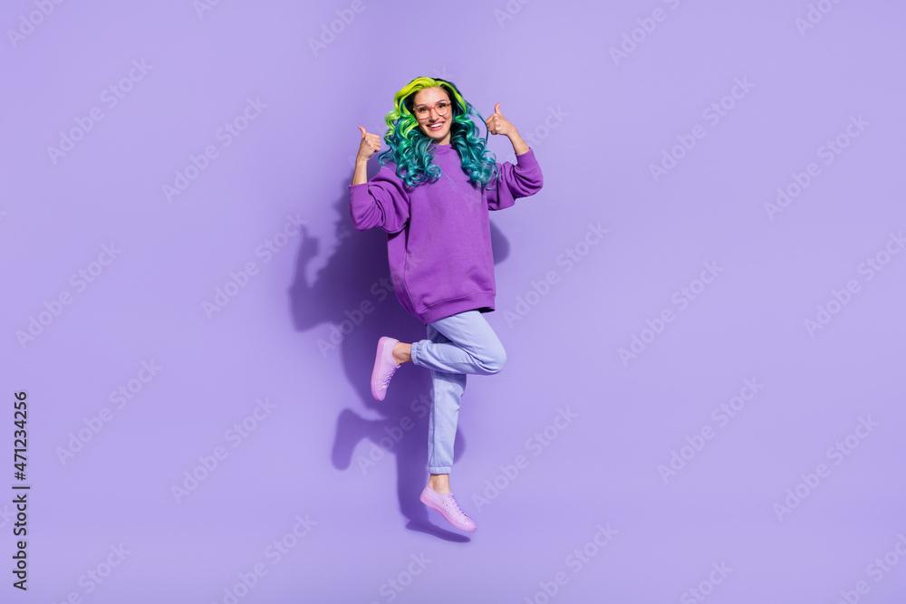 Full length photo of cheerful wavy curly haired lady jump up show thumbup symbol suggest ads isolated over purple color background