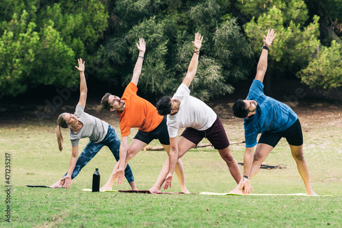 People doing the triangle pose of yoga in a park