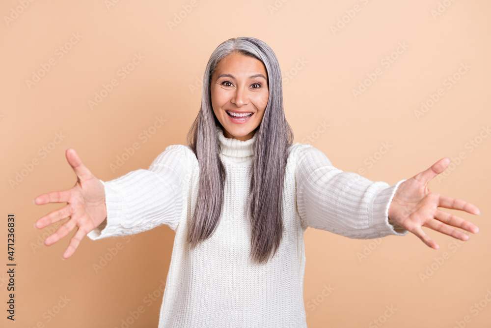 Photo of friendly cheerful pensioner lady stretch hands invite hug wear white sweater isolated beige color background Photo of friendly cheerful pensioner lady stretch hands invite hug wear white sweater isolated beige color background