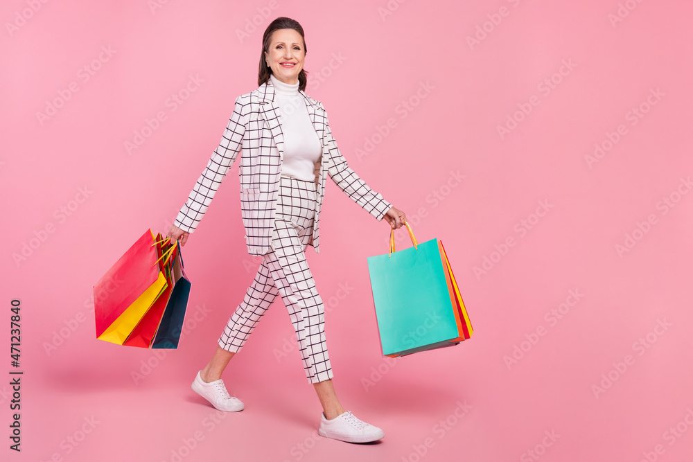 Full size photo of cheerful beautiful grandmother go shopping crazy shopaholic isolated on pink color background Full size photo of cheerful beautiful grandmother go shopping crazy shopaholic isolated on pink color background