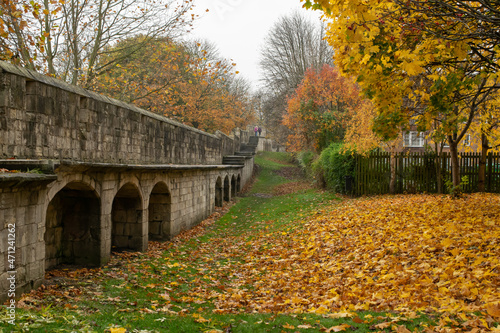 Part of medieval 13th century stone city wall with arches through colorful autumn foliage in York England photo