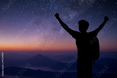 Silhouette of young traveler standing and open both arm watched night sky view  star and milky way alone on top of the mountain. He enjoyed traveling and was successful when he reached the summit.