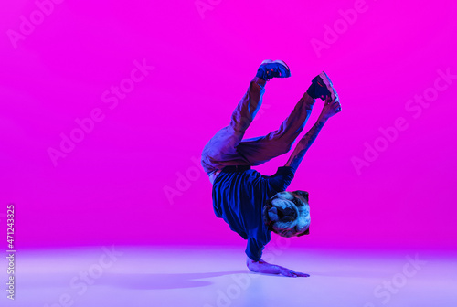Young man, break dancing dancer headed of dog's head dancing isolated over bright magenta background at dance hall in neon light.