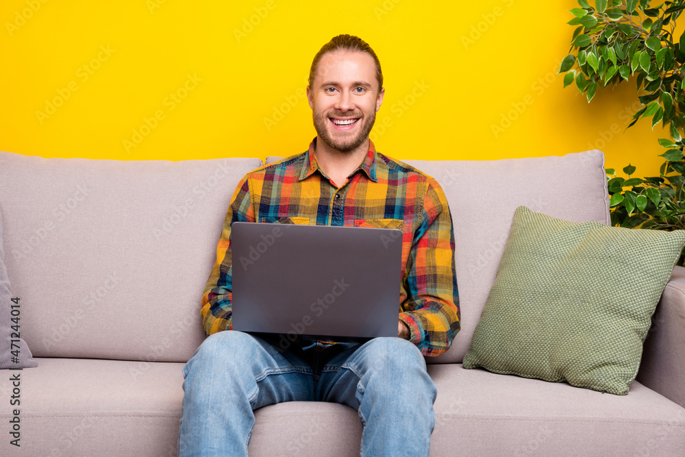 Photo of cheerful man sit couch hold netbook remote job concept wear plaid shirt isolated yellow color background Photo of cheerful man sit couch hold netbook remote job concept wear plaid shirt isolated yellow color background