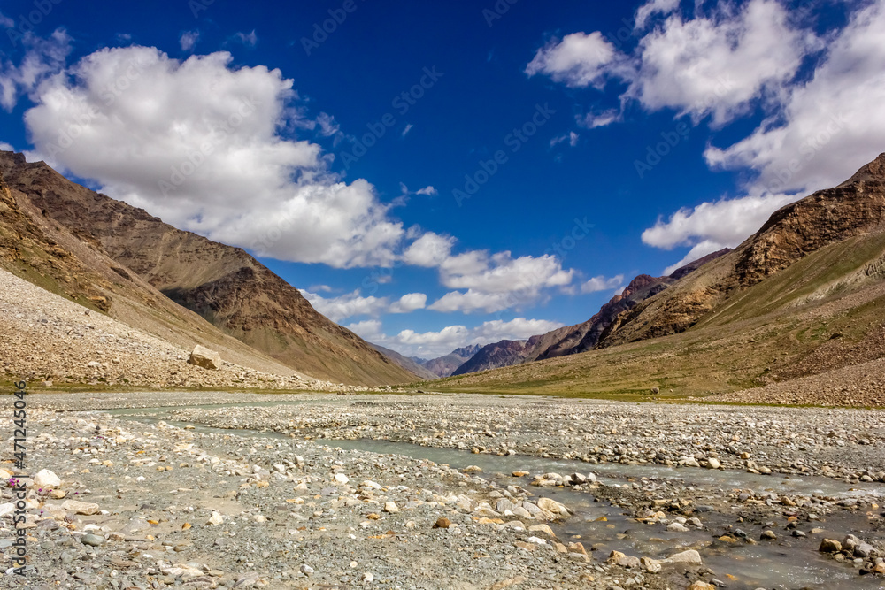 The wide river bed of the Kargyak river with the mountains of the Zanskar range and a blue sky on the Darcha Padum trekking route in the Indian Himalaya.