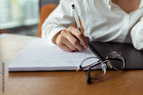 Unrecognizable crop businesswoman writing in notebook and making plan while working at table in cafe 
