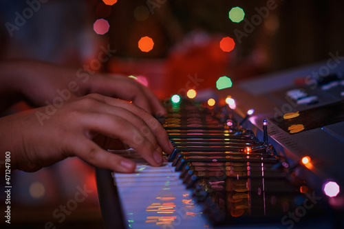 Christmas synthesizer on a dark background under the light of an electric garland. Close-up. Hands on the keys of a musical instrument. Merry Christmas, happy new year.