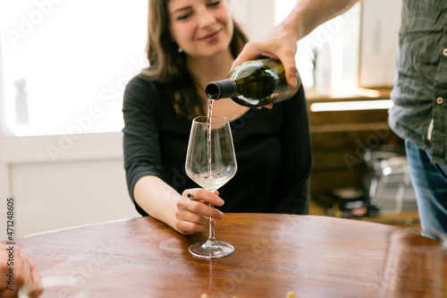man hand pouring white wine in the glass - female customer holding glass of wine at the cafe table photo