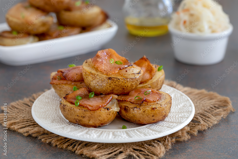 Halved potatoes baked with onion and chopped bacon. Portion served on a white plate with sauerkraut salad. Dark background, selective focus. Halved potatoes baked with onion and chopped bacon. Portion served on a white plate with sauerkraut salad. Dark background, selective focus.