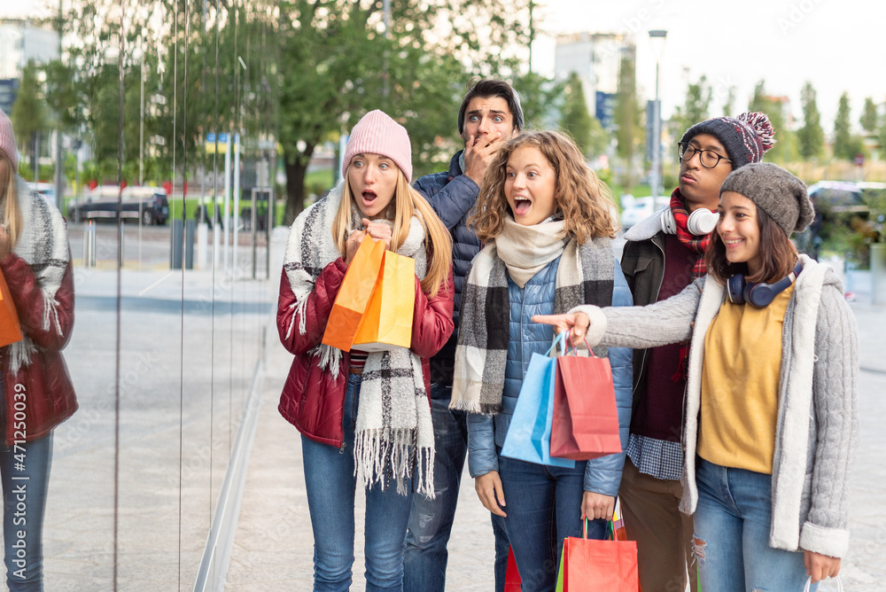 Fototapeta premium multiethnic group of friends around the city shopping, brunette woman showing the store windows, all smiling except the men who are bored, christmas time