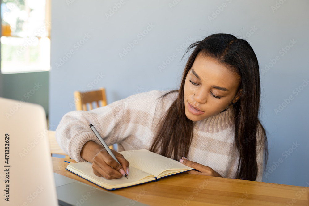 Online education, lifestyle and people concept - Close-up of an African-American girl with a laptop taking important notes in a workbook during an online conference at a coffee shop in quarantine Online education, lifestyle and people concept - Close-up of an African-American girl with a laptop taking important notes in a workbook during an online conference at a coffee shop in quarantine
