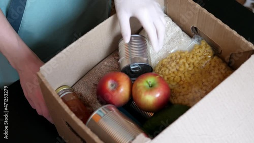 Gloved volunteer collects a box of food for those in need. Social assistance during the coronavirus COVID-19. The concept of social assistance, charity, donation