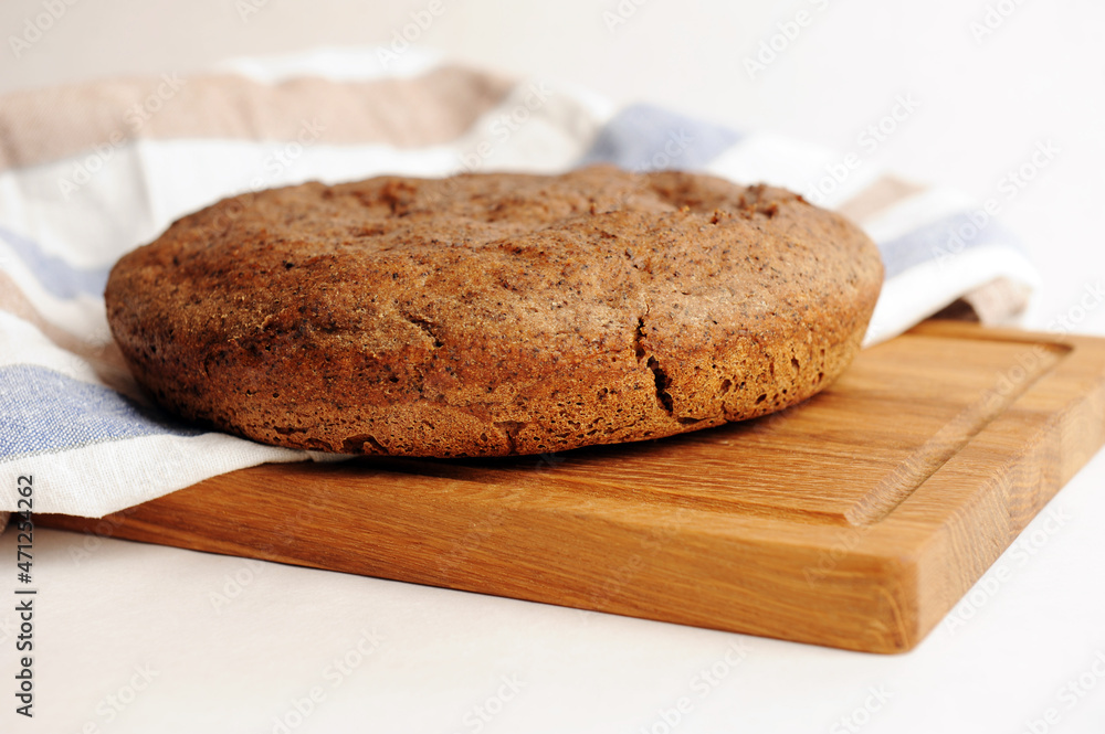 Fresh homemade round malted rye bread on wooden board. White background, linen fabric