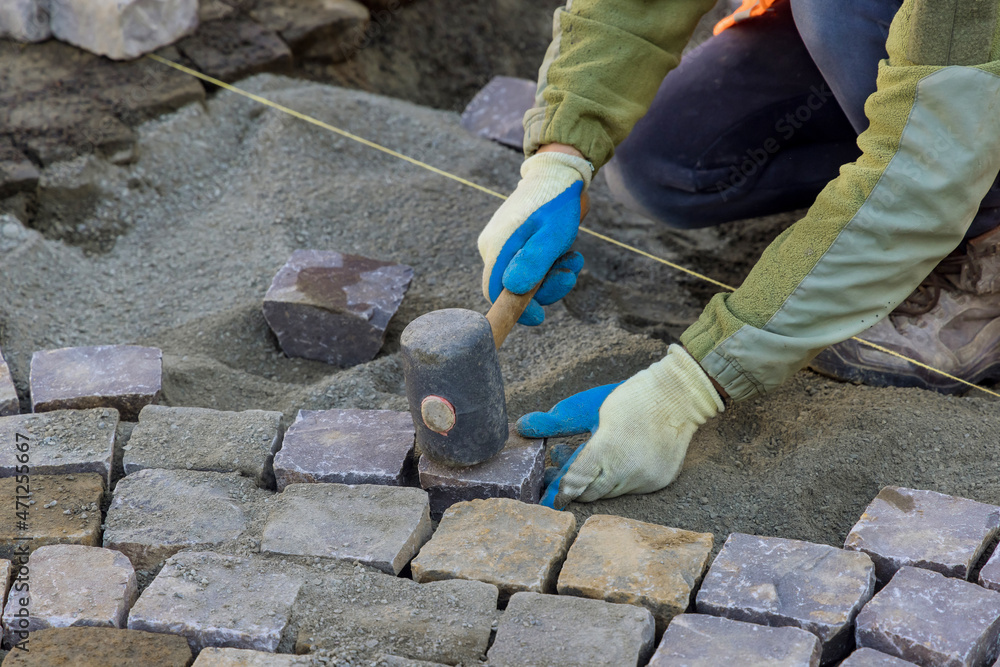 Worker using rubber hammer to laying pavement stones on sidewalk near road in city Worker using rubber hammer to laying pavement stones on sidewalk near road in city