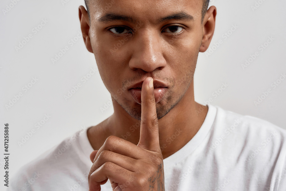 Portrait of dark skinned young guy showing shh gesture, keeping a secret, posing isolated over white background Portrait of dark skinned young guy showing shh gesture, keeping a secret, posing isolated over white background