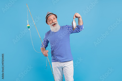 Portrait of attractive cheerful grey-haired man holding rod fresh fish food carp isolated over bright blue color background