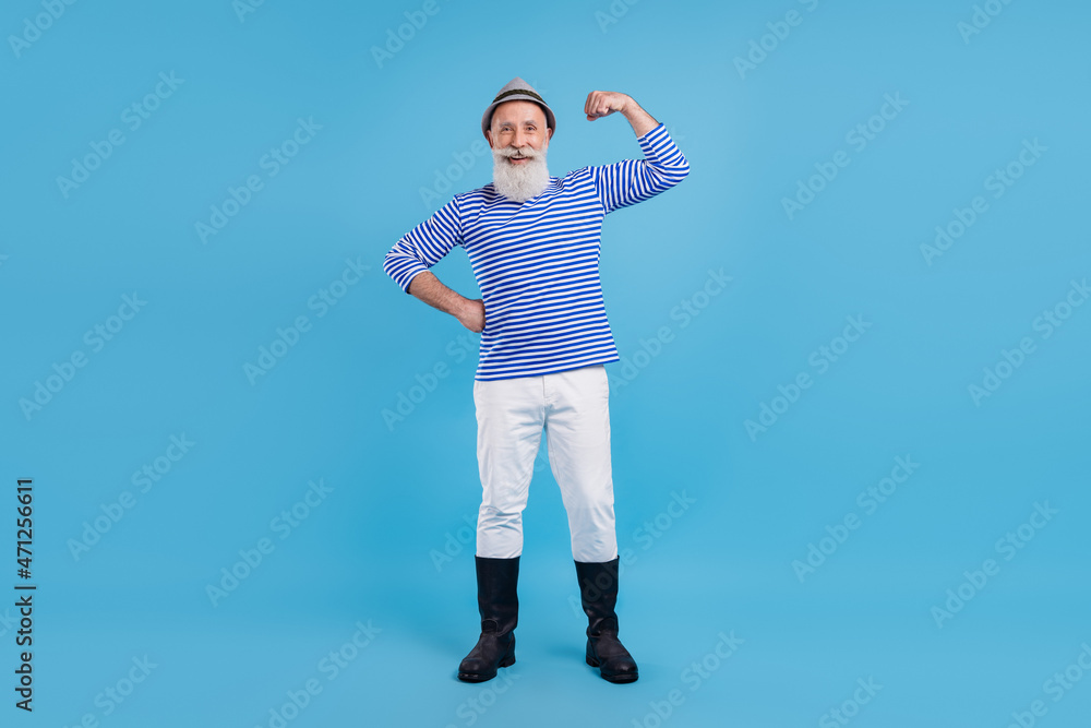 Full length body size view of trendy cheerful grey-haired man demonstrating biceps posing isolated over bright blue color background Full length body size view of trendy cheerful grey-haired man demonstrating biceps posing isolated over bright blue color background