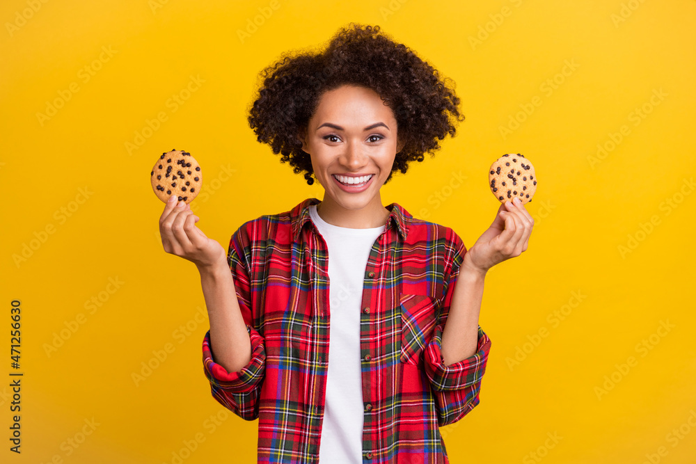 Portrait of attractive cheerful girl holding in hands fresh delicious cookies isolated over bright yellow color background