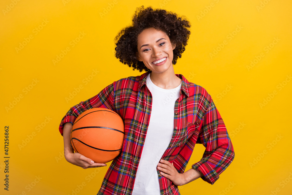 Portrait of attractive cheerful girl holding basketball ball active day isolated over bright yellow color background