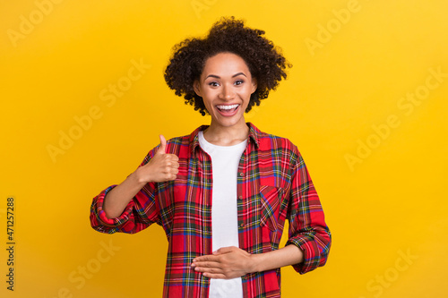 Portrait of attractive cheerful girl showing thumbup touching stomach isolated over bright yellow color background