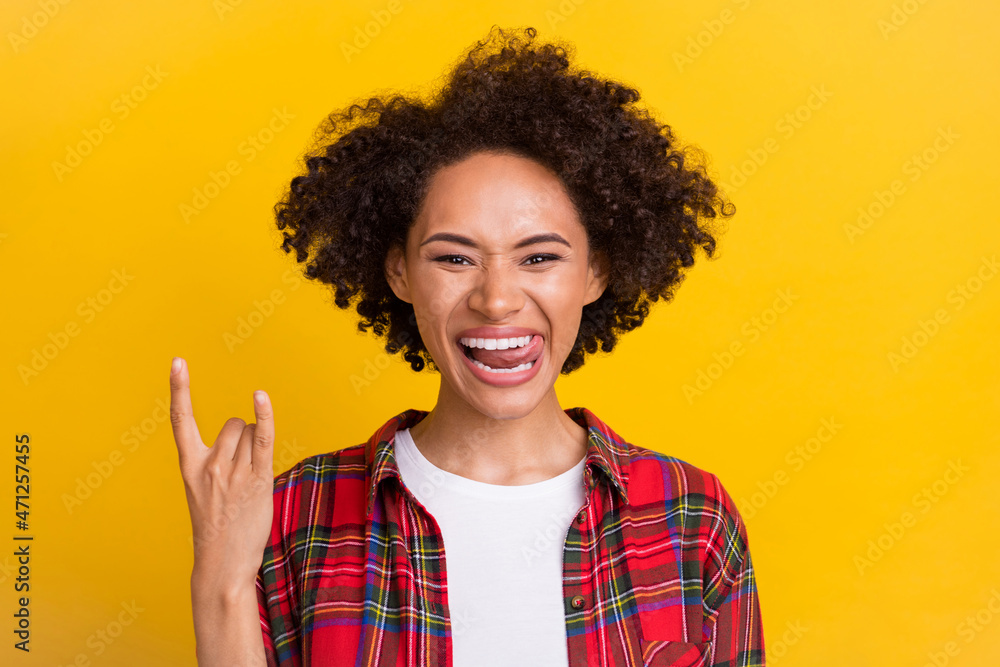 Portrait of attractive cheerful funny girl showing horn sign having fun isolated over bright yellow color background Portrait of attractive cheerful funny girl showing horn sign having fun isolated over bright yellow color background