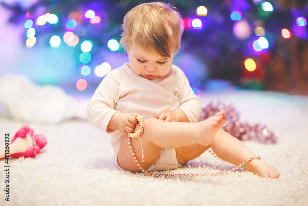 Adorable baby girl holding pink Christmas tree beads in cute hands. Little child playing and decorating xmas tree with family. First celebration. Toddler and colorful lights on background. Adorable baby girl holding pink Christmas tree beads in cute hands. Little child playing and decorating xmas tree with family. First celebration. Toddler and colorful lights on background.