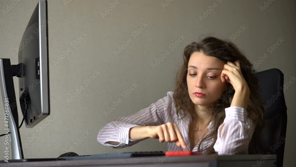 Tired young woman with curly hair and white shirt is working at the office and using her red smartphone, routine work, freelance, burnout syndrome Tired young woman with curly hair and white shirt is working at the office and using her red smartphone, routine work, freelance, burnout syndrome