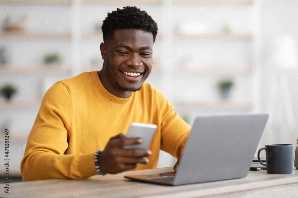 Young black man entrepreneur working on laptop and using cellphone Young black man entrepreneur working on laptop and using cellphone