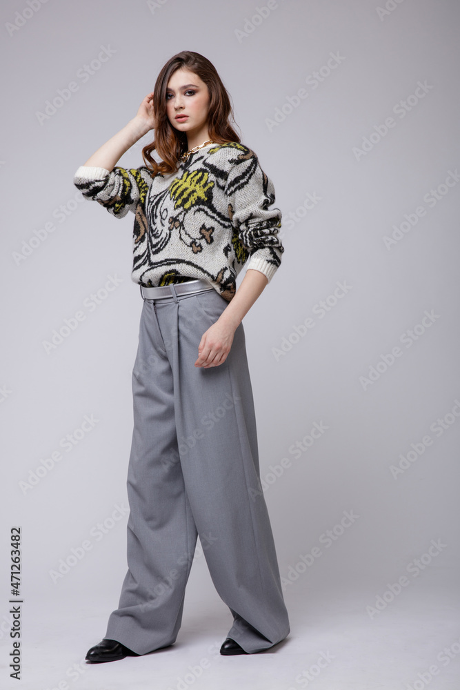 Fashion photo of a beautiful elegant young woman in a pretty gray pants, trousers, blouse, bicolor accessories, boots posing over white, soft gray background. Brown hair. Studio Shot. Fashion photo of a beautiful elegant young woman in a pretty gray pants, trousers, blouse, bicolor accessories, boots posing over white, soft gray background. Brown hair. Studio Shot.