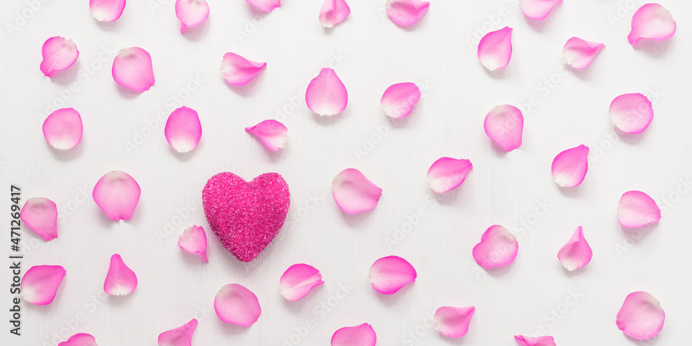 Valentine's Day. Pink heart decorated with rose petals on a white wooden background. Top view, flat lay. Wide composition.