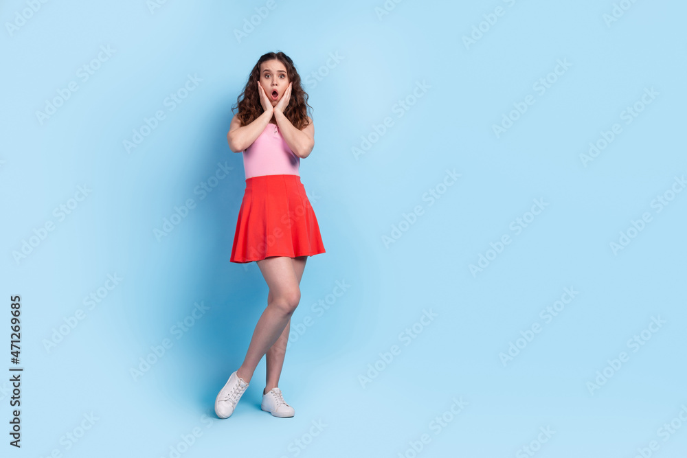 Full body photo of young woman arms touch cheeks amazed stupor panic fake news isolated over blue color background Full body photo of young woman arms touch cheeks amazed stupor panic fake news isolated over blue color background