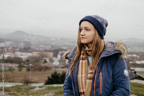 Beautiful young woman in blue coat, scarf and hat. Wet hair at rainy day in Norway. City in background.