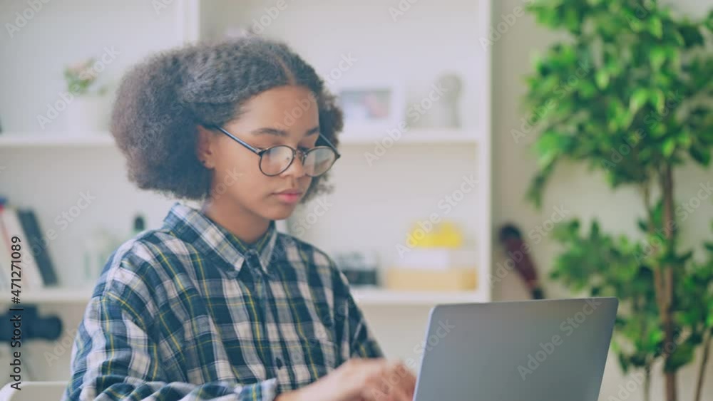 Smart black teen girl in eyeglasses opening laptop, doing homework for school Smart black teen girl in eyeglasses opening laptop, doing homework for school