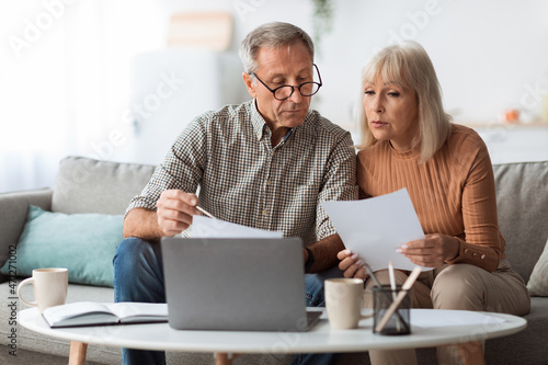 Senior Couple Looking Through Papers Counting Reading Bills At Home