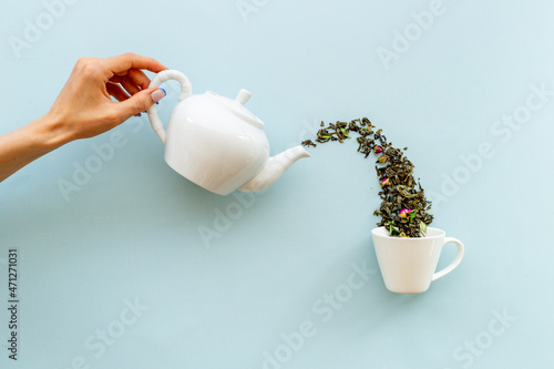 Female hand pours tea leaves from teapot in cup
