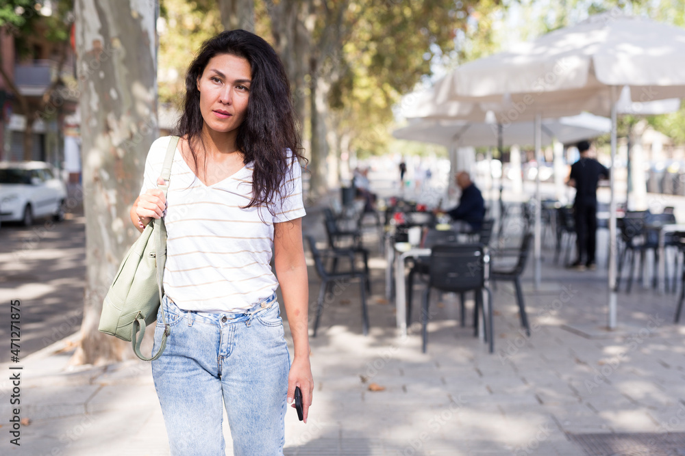  woman with shoulder bag walking near outdoor cafe.