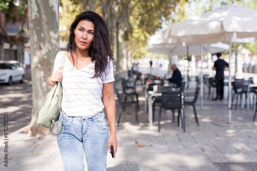  woman with shoulder bag walking near outdoor cafe. © JackF