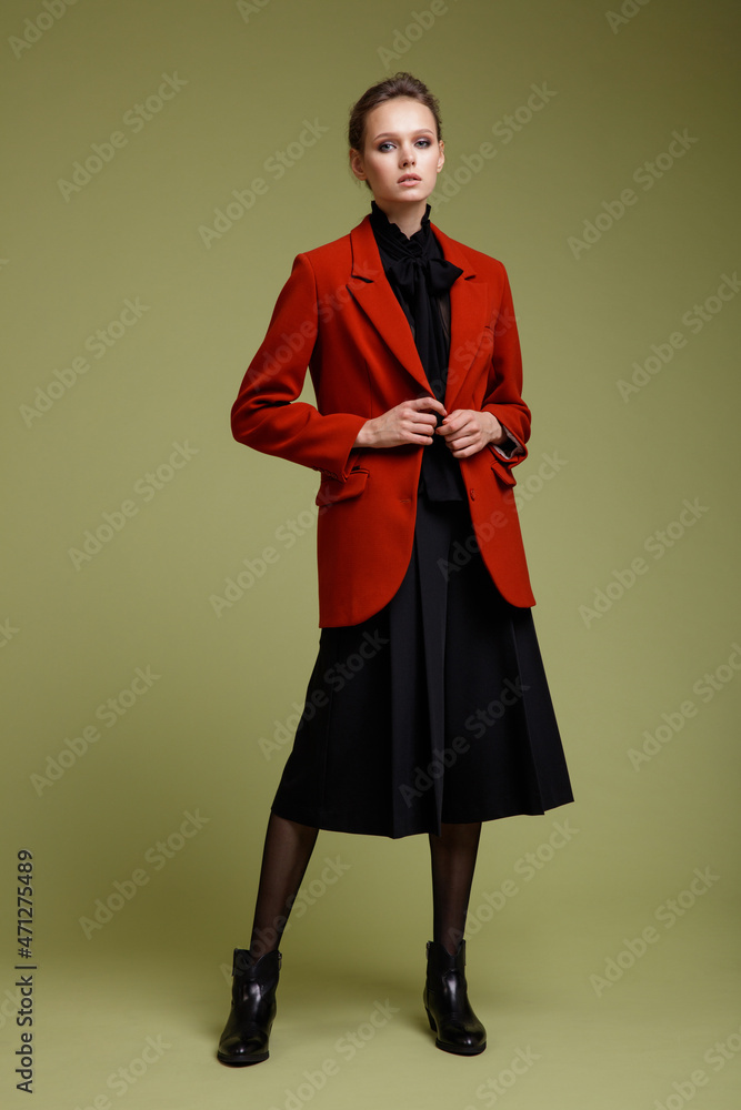 Fashion photo of a beautiful elegant young woman in a pretty suit, red jacket, black transparent blouse, short pants posing over green background. Studio Shot. Full length portrait Fashion photo of a beautiful elegant young woman in a pretty suit, red jacket, black transparent blouse, short pants posing over green background. Studio Shot. Full length portrait