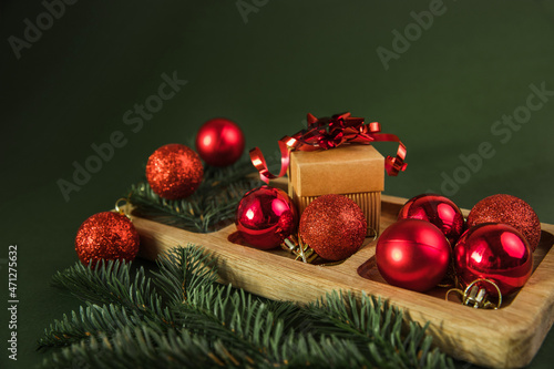 Top view of festive wood plate with red baubles, Christmas tree and gifts on green background. Christmas decorations and toys. New Year advent concept. Close-up