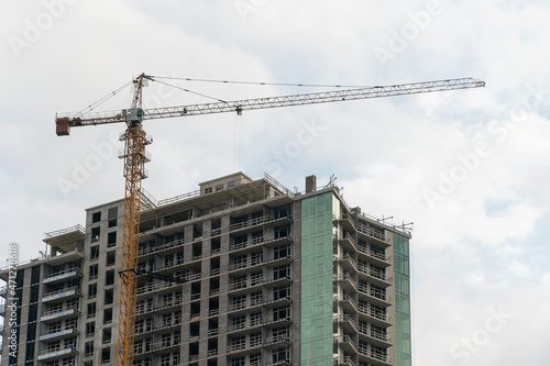 Construction crane on the background of a multi-storey building under construction on a cloudy day