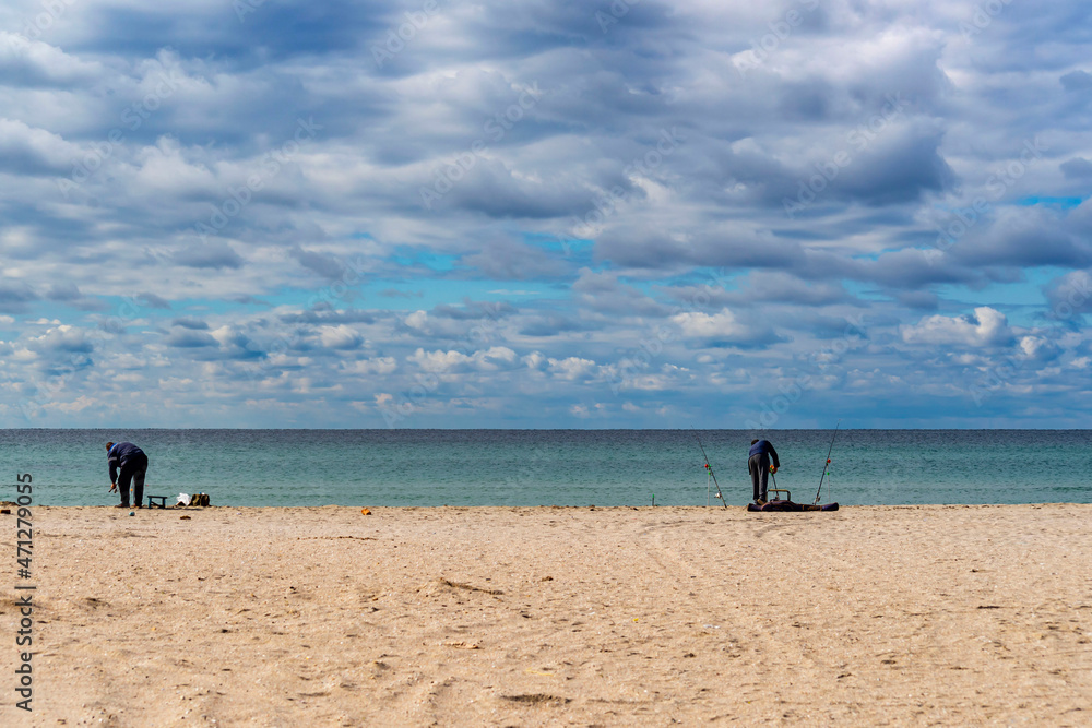 Fishermen catch fish on the sandy shore of the Sea with fishing rods