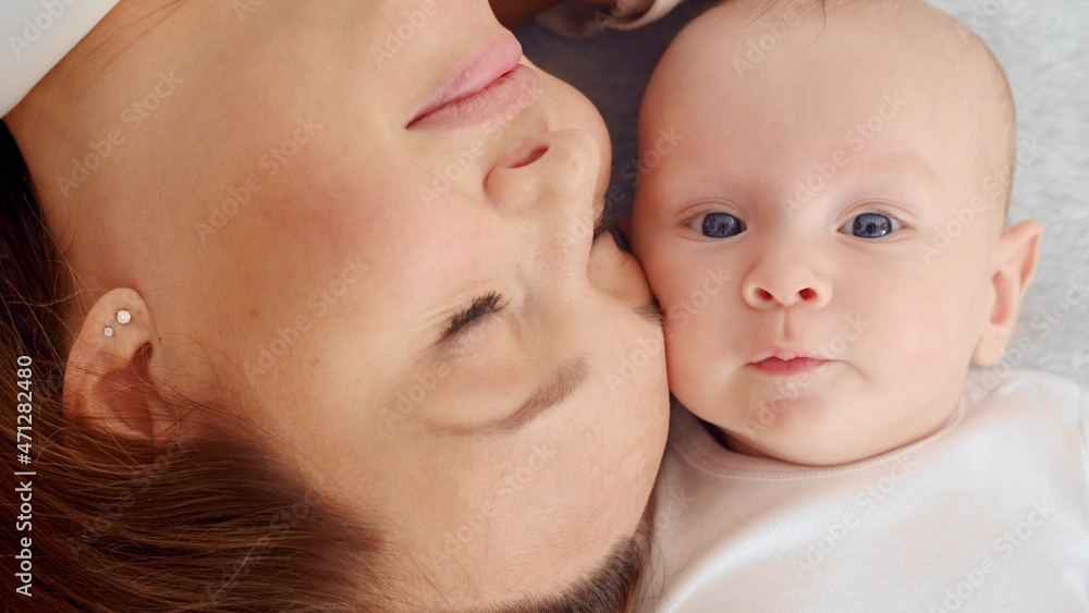 Happy newborn baby with his mother. Healthy newborn baby in a white t-shirt with mom. Closeup Faces of the mother and infant baby. Cute Infant boy and parent, top view. Happy family portrait Happy newborn baby with his mother. Healthy newborn baby in a white t-shirt with mom. Closeup Faces of the mother and infant baby. Cute Infant boy and parent, top view. Happy family portrait