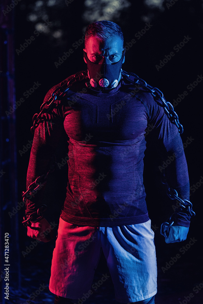 Young tough muscular man with training mask and workout chains around his torso giving you a staredown scary look as he takes a break from a hard strength training in the park Young tough muscular man with training mask and workout chains around his torso giving you a staredown scary look as he takes a break from a hard strength training in the park