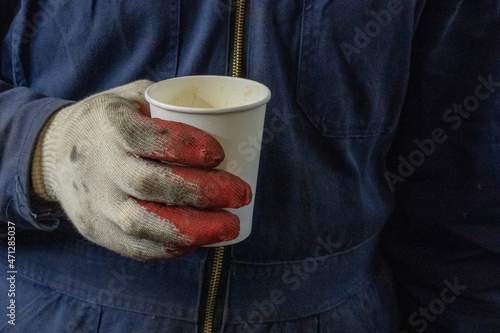 Photo of a white paper cup of coffee in the hands in gloves of a male worker