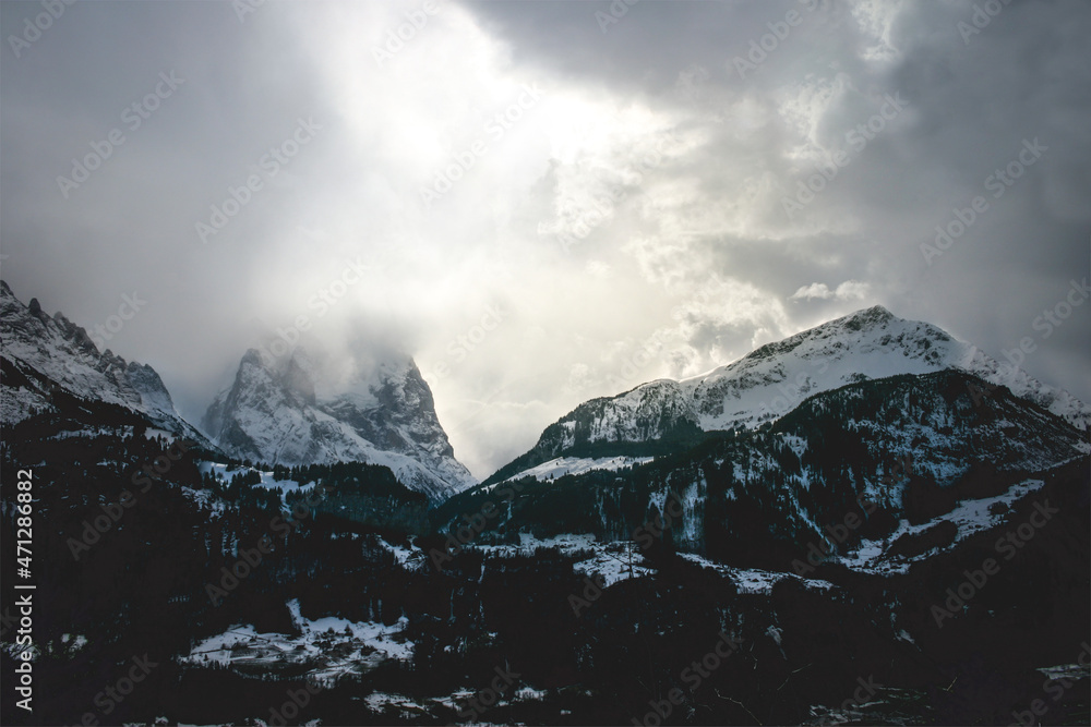 intense mood mountain range in switzerland alps, strong clouds and bright light at midday