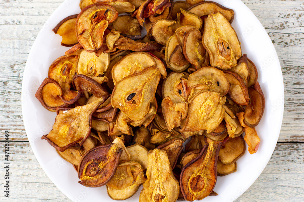 A pile of dried pears in slices on a white plate on wooden background. Dried fruit chips. Healthy food A pile of dried pears in slices on a white plate on wooden background. Dried fruit chips. Healthy food
