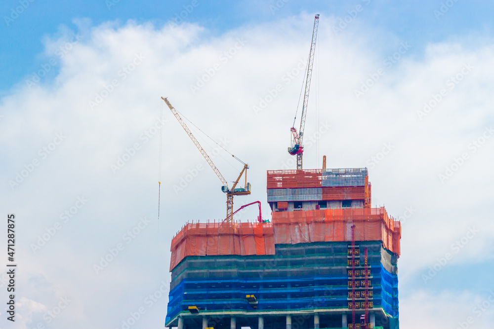Fototapeta premium Operated tower construction cranes on the roof top of skyscraper against the blue sky background. Industrial background construction.