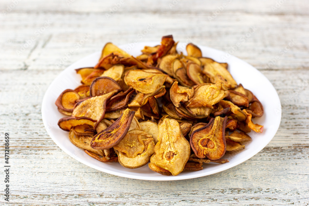 A pile of dried pears in slices on a white plate on wooden background. Dried fruit chips. Healthy food